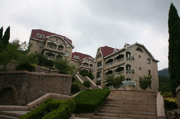 爱尊客度假山庄是爱尊客连锁酒店开辟的以旅游度假的会议为主体的商务酒店。是一座将欧美式风格、中国古典建筑风格与现代文化气息融为一体的园林式建筑。位于风景秀丽的崂山北九水风景区,距市区仅40分钟路程九水十八潭,远离喧嚣的都市,山舒水美,是新闻单位,企业等培训,笔会,团体会议,和休闲度假的首选之地。山庄占地面积8000多平方米建筑面积4000多平方米依水而建的六栋楼错落有致,玲珑秀美,为著名的崂山添了一道亮丽的风景,身在其中,崂山独有的怪、秀、奇、幽、深、巨、雅的迷人景观尽收眼底犹如仙境。 地址
