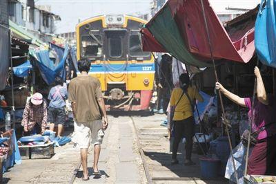 2014年4月21日，泰國美功，小販趕在火車到來前收拾貨物。泰國鐵路十分老舊，全部為窄軌鐵路，時速僅50公里左右，在貧民區(qū)經(jīng)常能見到鐵道市場。