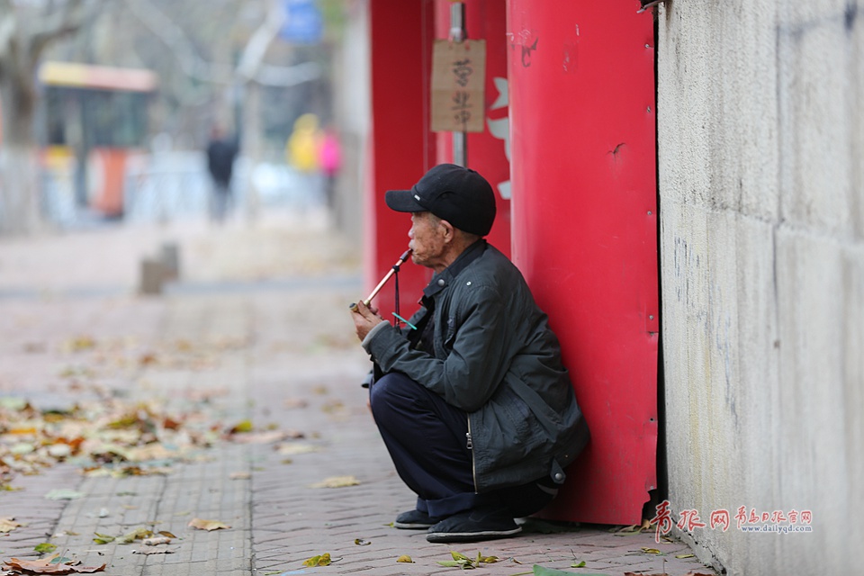 沂水路附近,一位老人蹲在墙角抽烟.